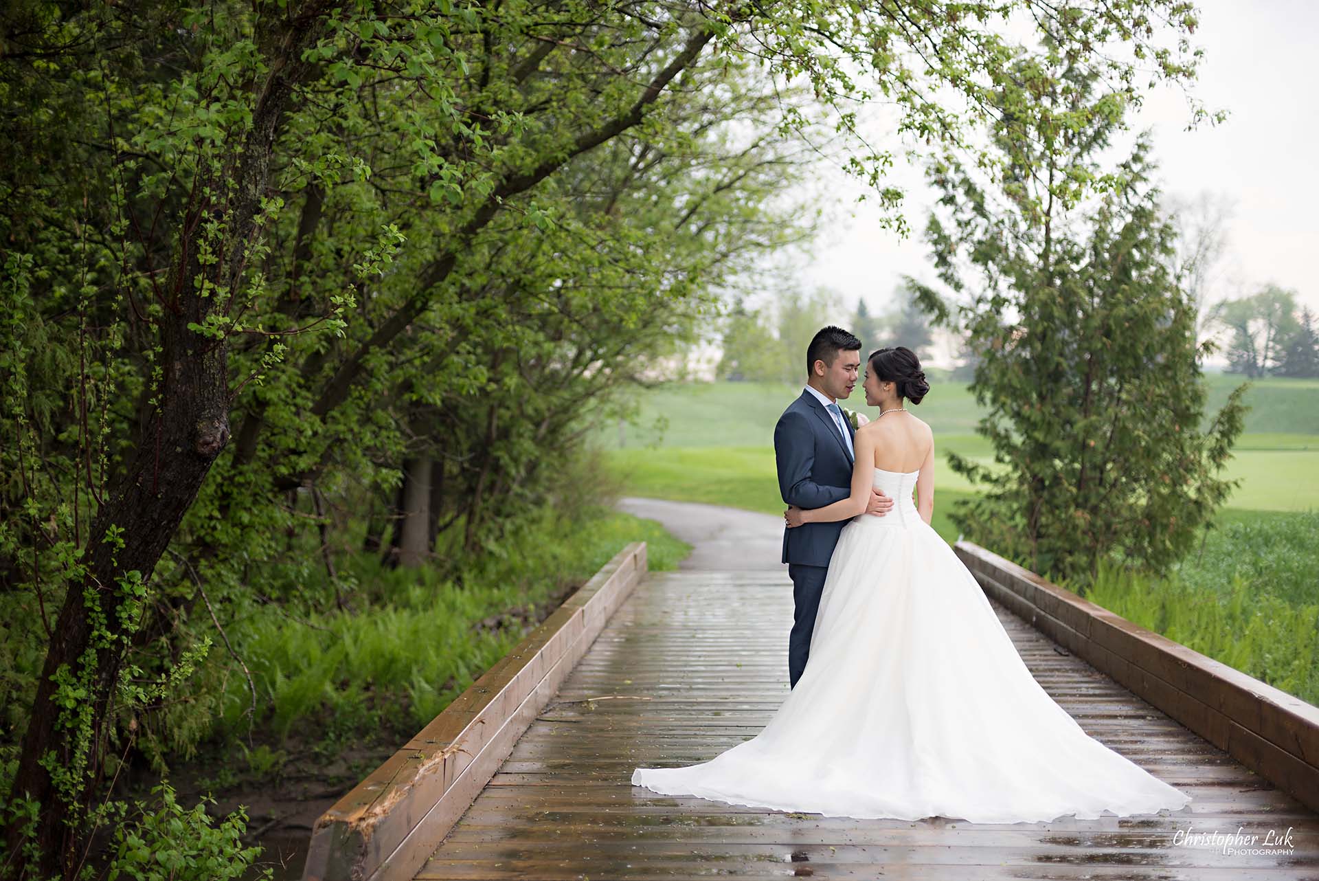 Christopher Luk Toronto Wedding Photographer Angus Glen Golf Club Markham Great Hall Dinner Reception Event Venue Green Field Sunset Bride Groom Natural Candid Photojournalistic Wooden Bridge Green Arch Trees Holding Each Other Hug Bridal Dress Gown Train Landscape