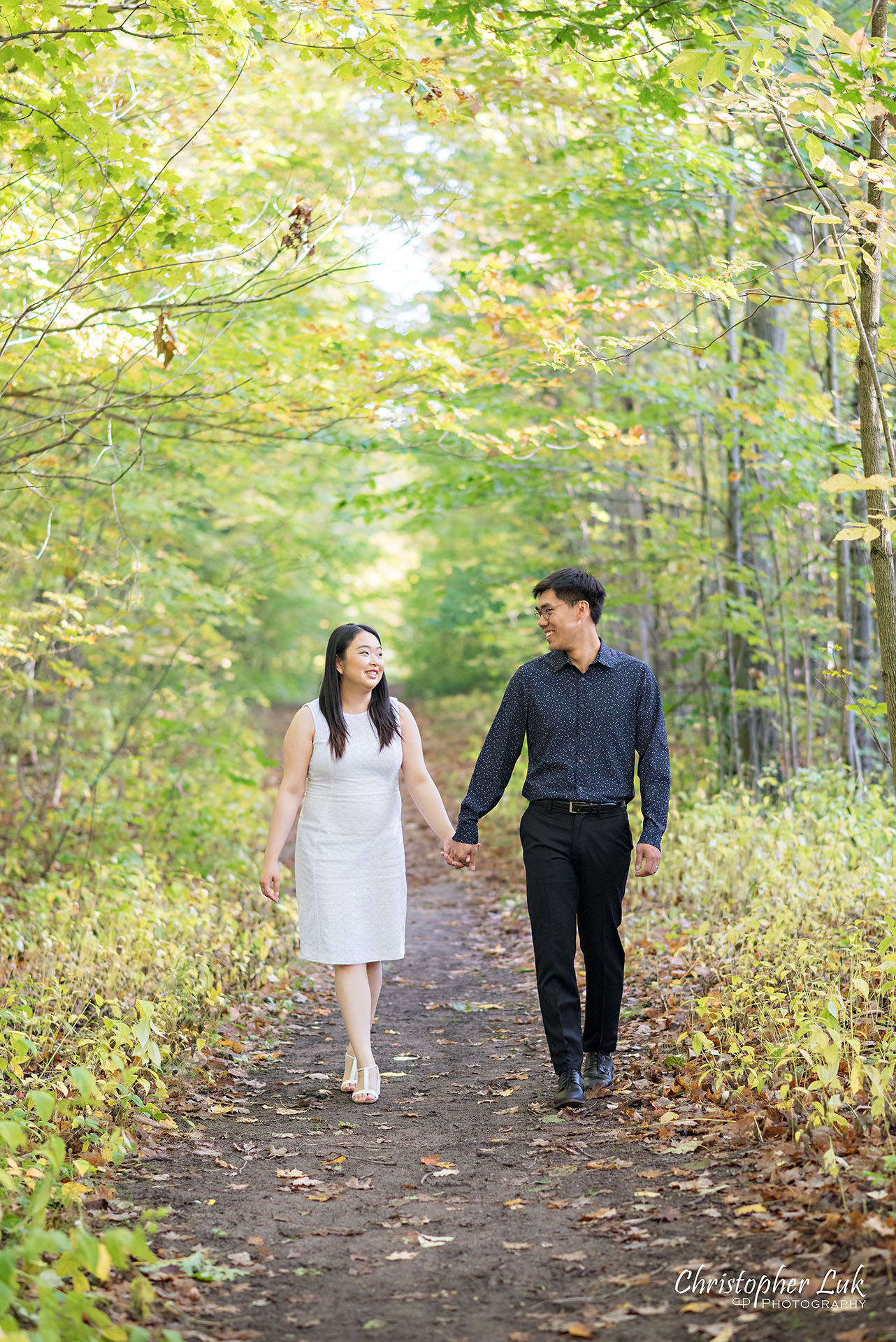 Christopher Luk Toronto Wedding Photographer Stouffville Forest Conservation Park Engagement Session Candid Natural Photojournalistic Bride Groom Walking Together Trail Smile Pond Autumn Fall Leaves Vertical