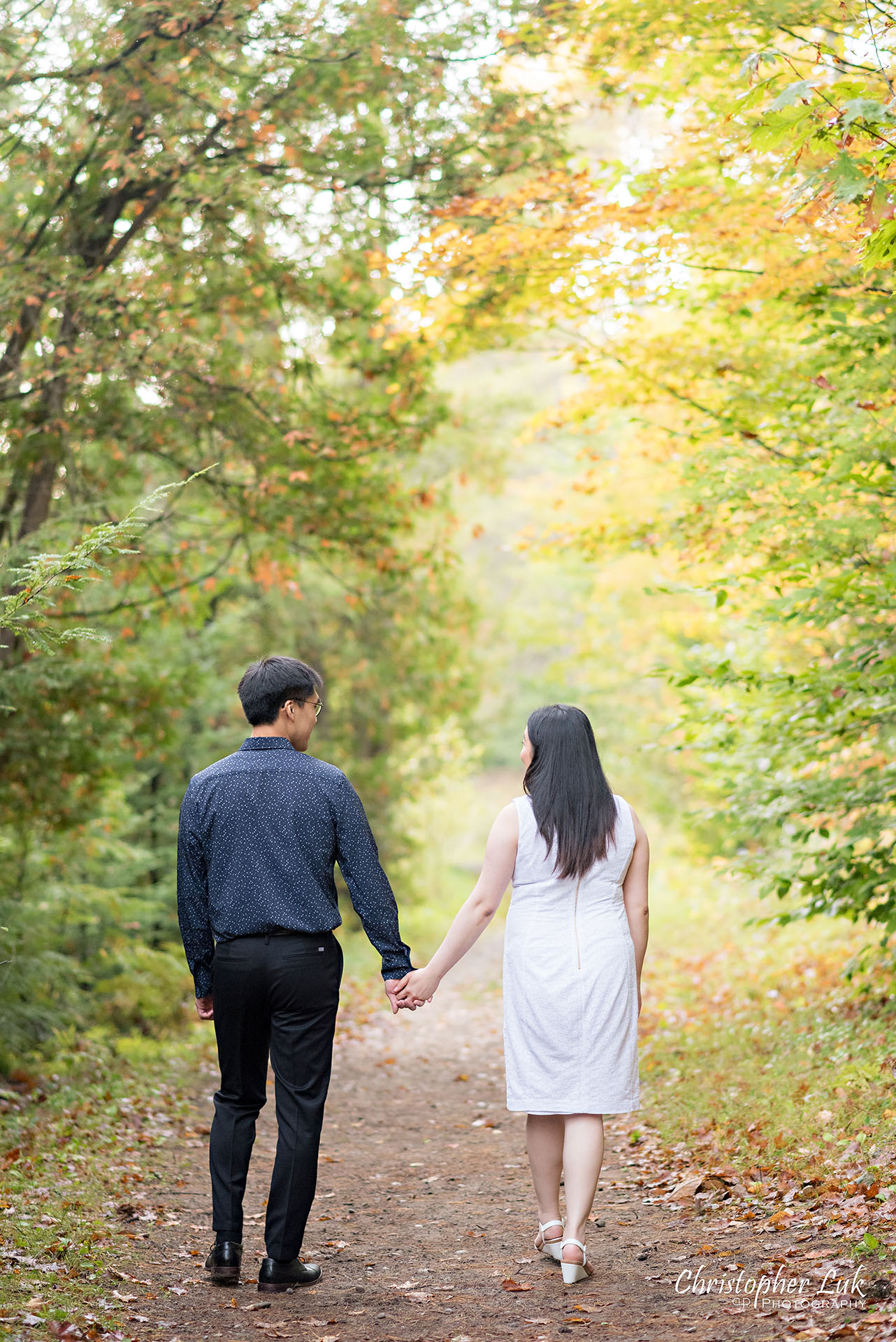 Christopher Luk Toronto Wedding Photographer Stouffville Forest Conservation Park Engagement Session Candid Natural Photojournalistic Bride Groom Walking Together Holding Hands Autumn Fall Leaves Vertical