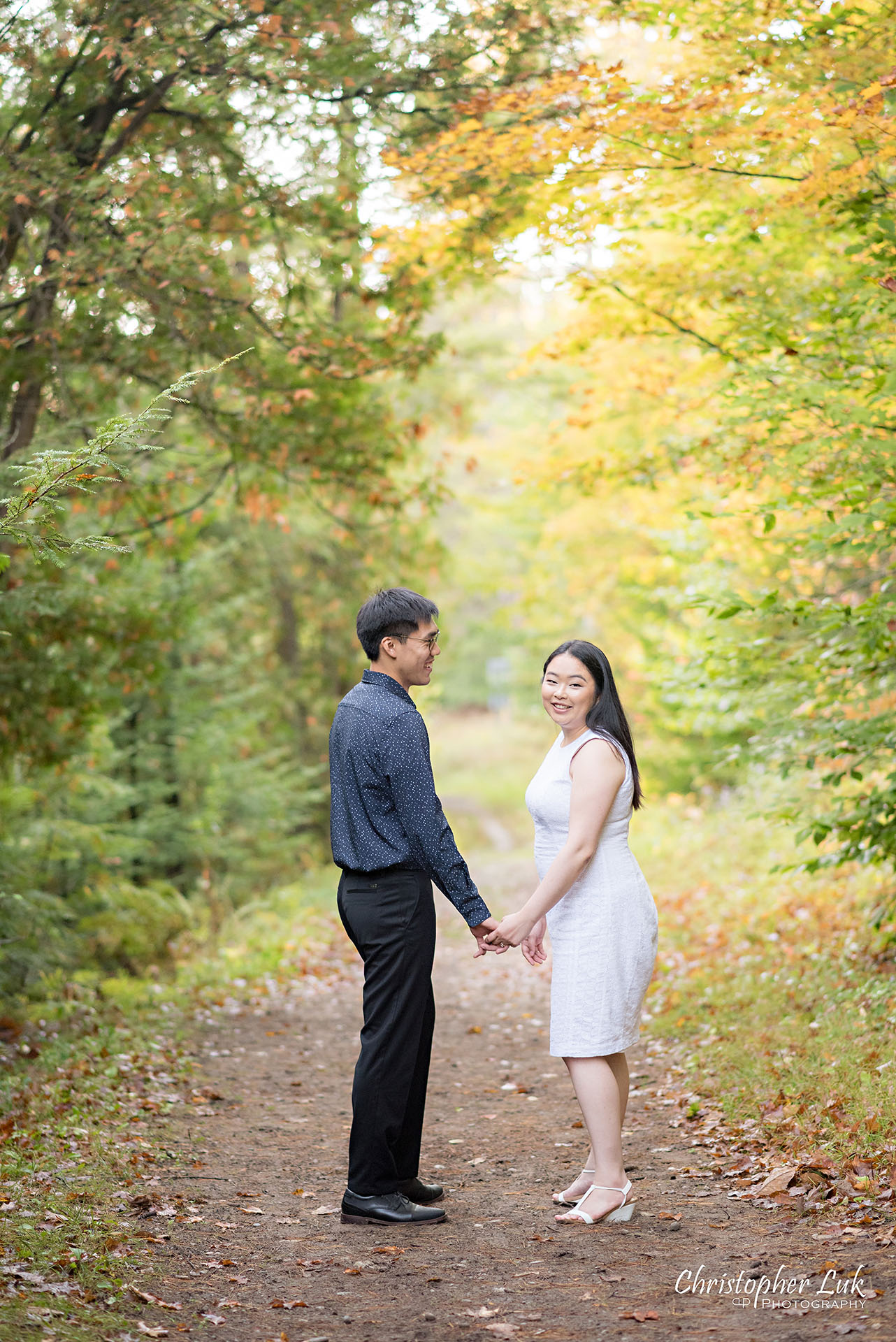 Christopher Luk Toronto Wedding Photographer Stouffville Forest Conservation Park Engagement Session Candid Natural Photojournalistic Bride Groom Walking Together Holding Hands Autumn Fall Leaves Smile Vertical