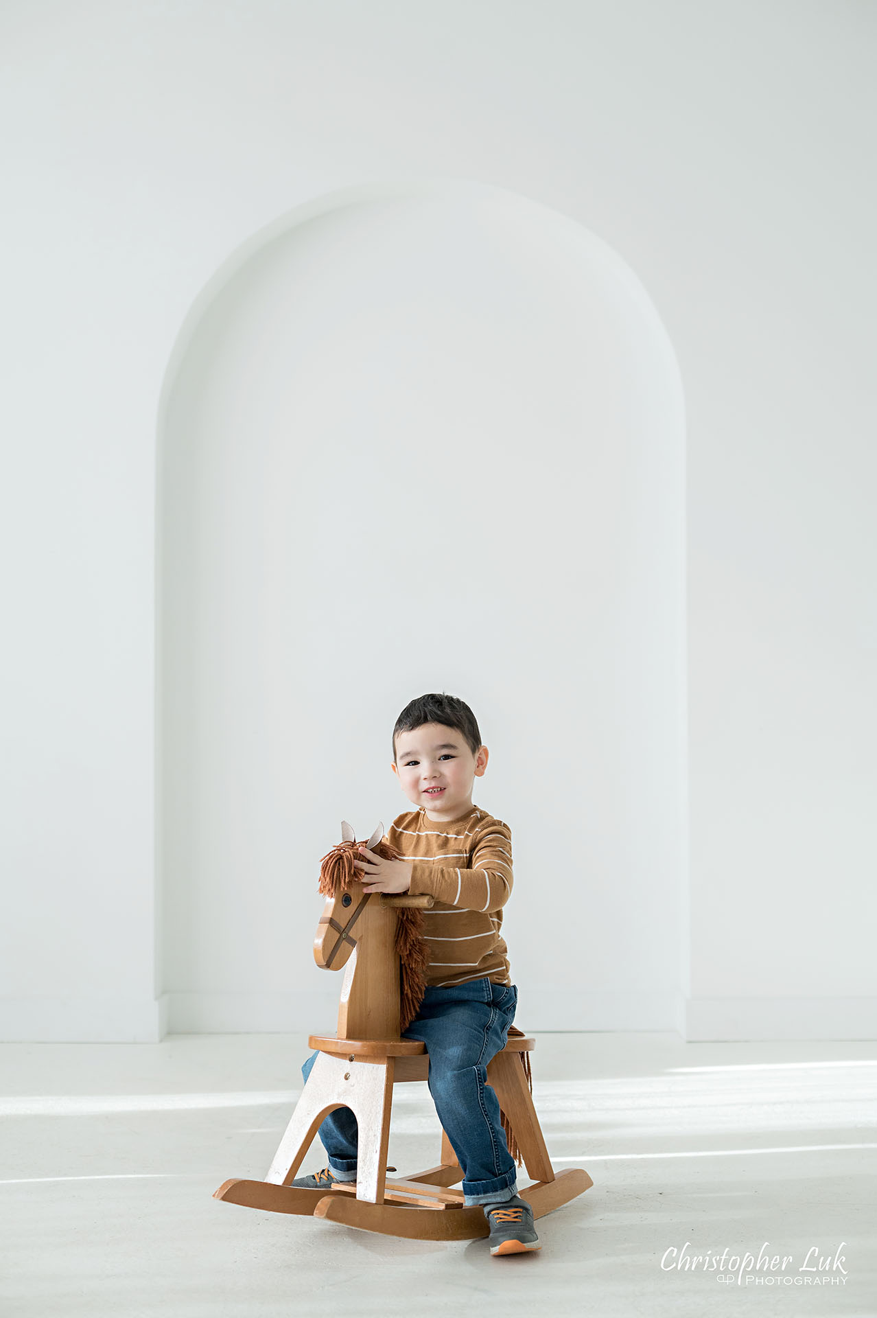 Son Brother Toddler Child Playing Wooden Rocking Horse Family Studio Portrait Candid Natural Photojournalistic