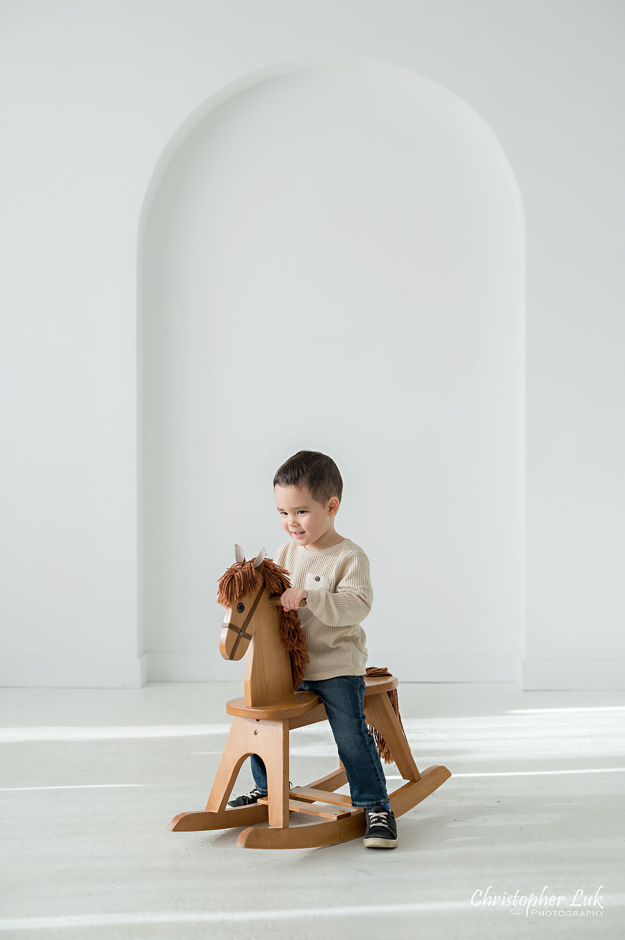 Son Brother Toddler Child Playing Wooden Rocking Horse Family Studio Portrait Candid Natural Photojournalistic